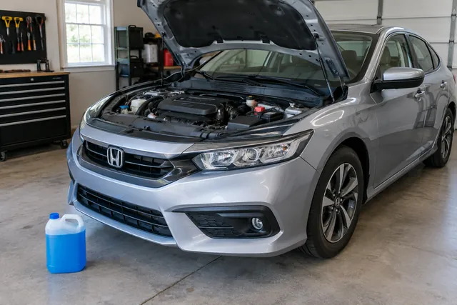 Blue coolant in a sealed jug beside a parked Honda with its hood open and engine off