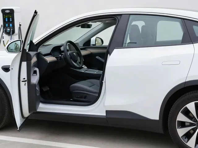 Electric car connected to a charger with its dashboard and odometer visible through an open door