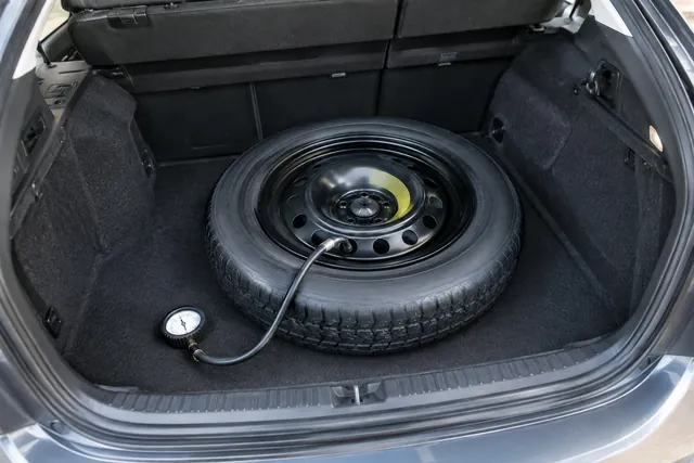 Tire pressure gauge attached to the valve of a compact spare tire in an open trunk