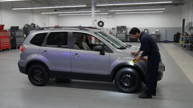 Subaru parked in a service bay with a technician inspecting the wheel area