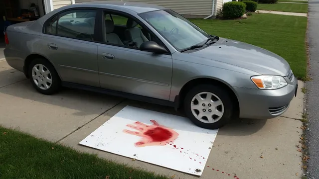 Reddish fluid on white cardboard beneath the front of a parked car