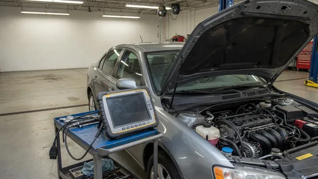 Diagnostic scanner beside a parked vehicle with its hood open in an automotive workshop
