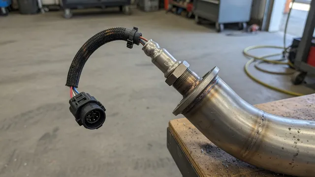 Illustration of an upstream wideband oxygen sensor, its connector, and wiring near an exhaust pipe