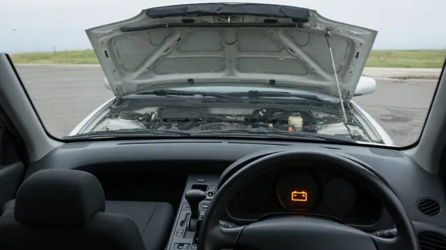 Car dashboard with an illuminated battery warning light and an engine bay visible beyond the windshield