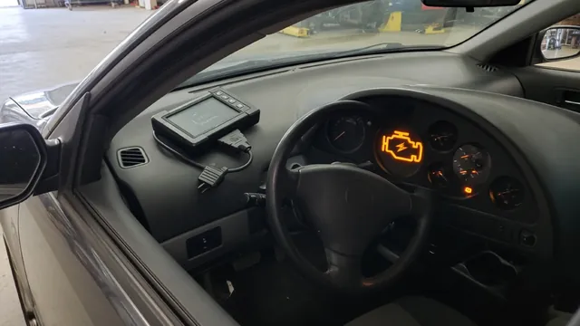 Diagnostic scanner beside a vehicle dashboard with an illuminated check engine light